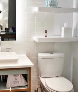 A small bathroom with wall shelves above the toilet